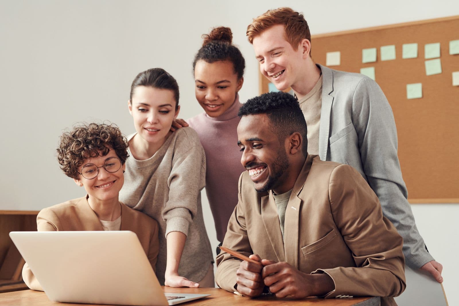 A group of colleagues gathered around a laptop, talking and smiling.