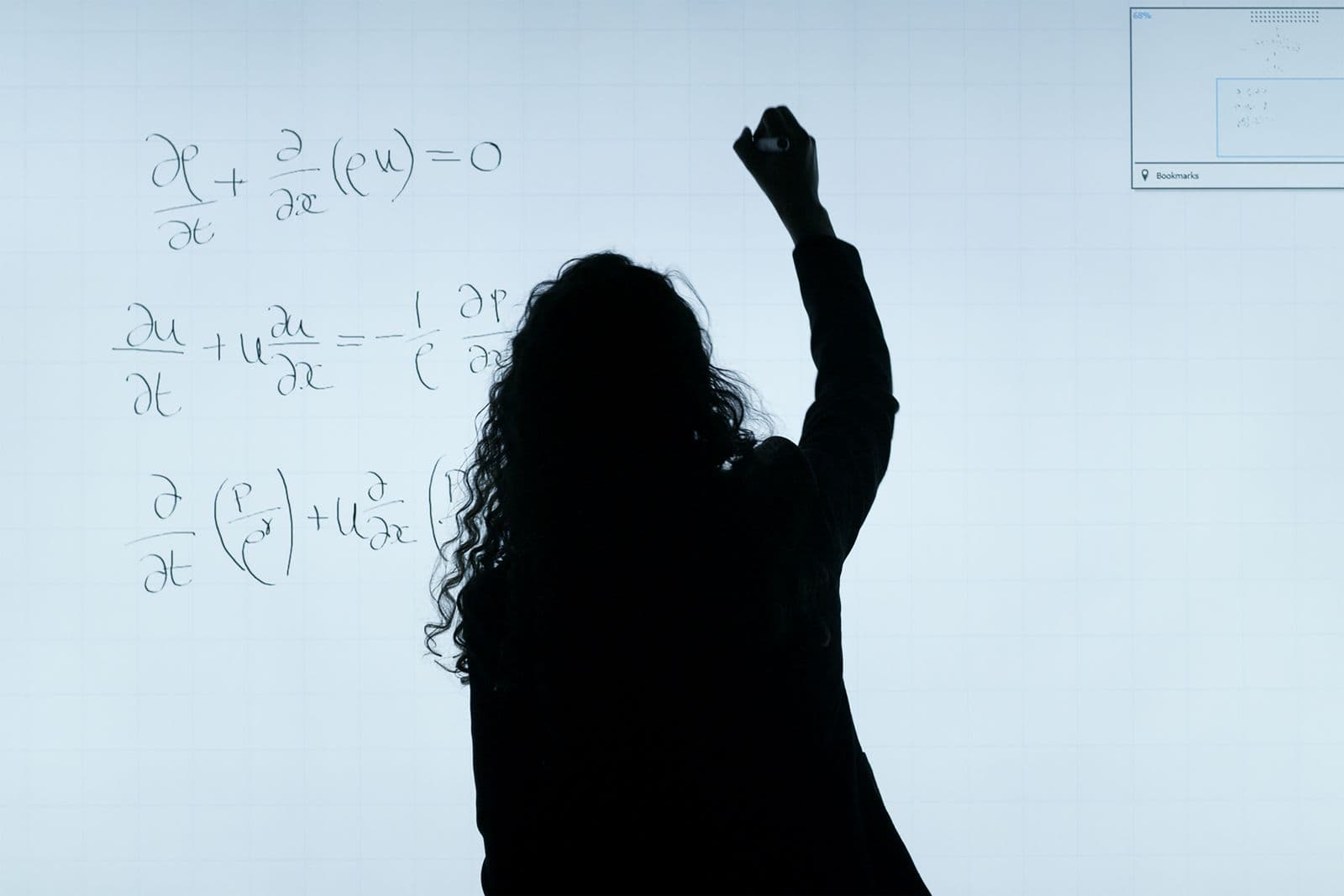 A person writing equations on a large whiteboard, seen in silhouette.