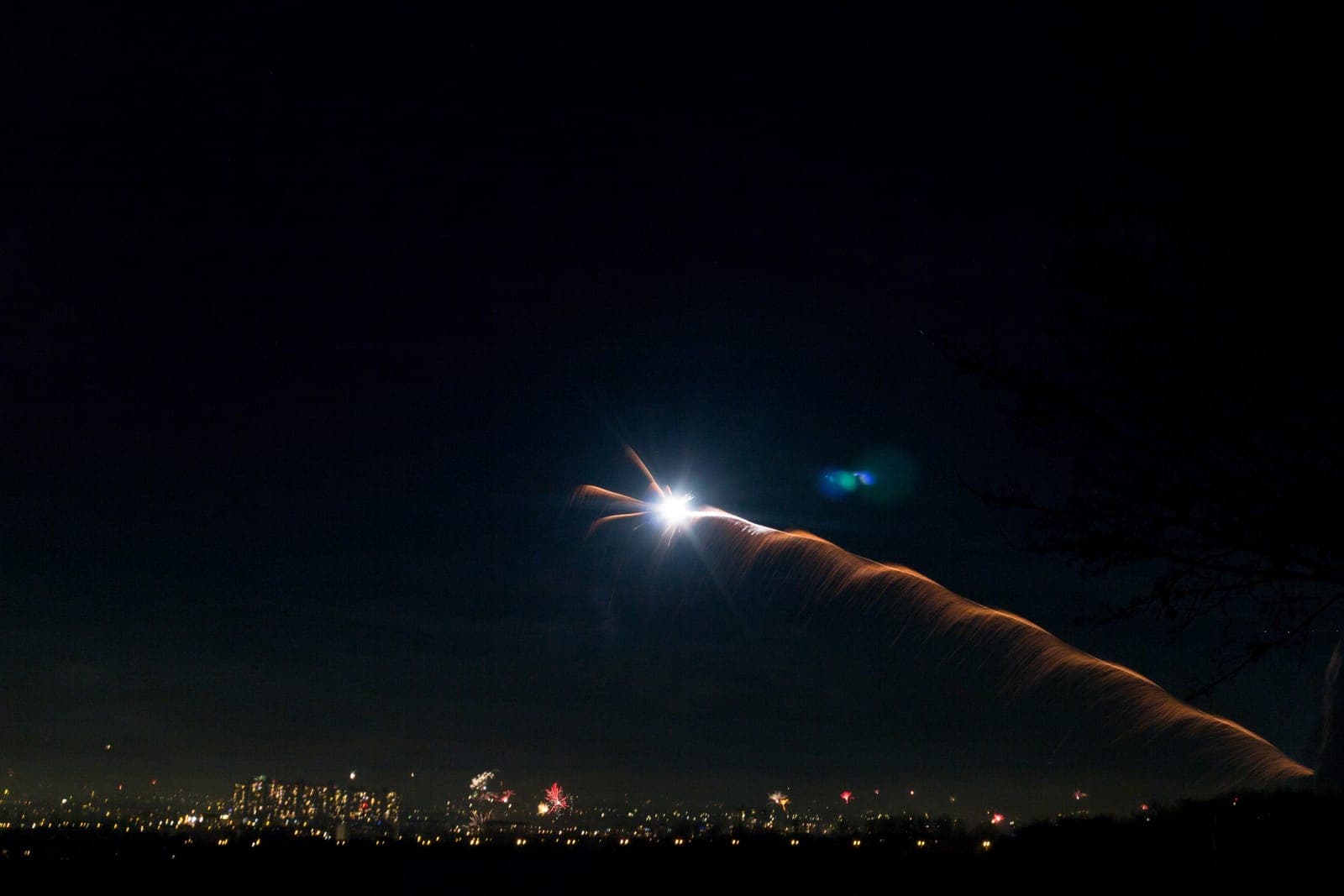 A bright launch trail arcing across a night sky above city lights.